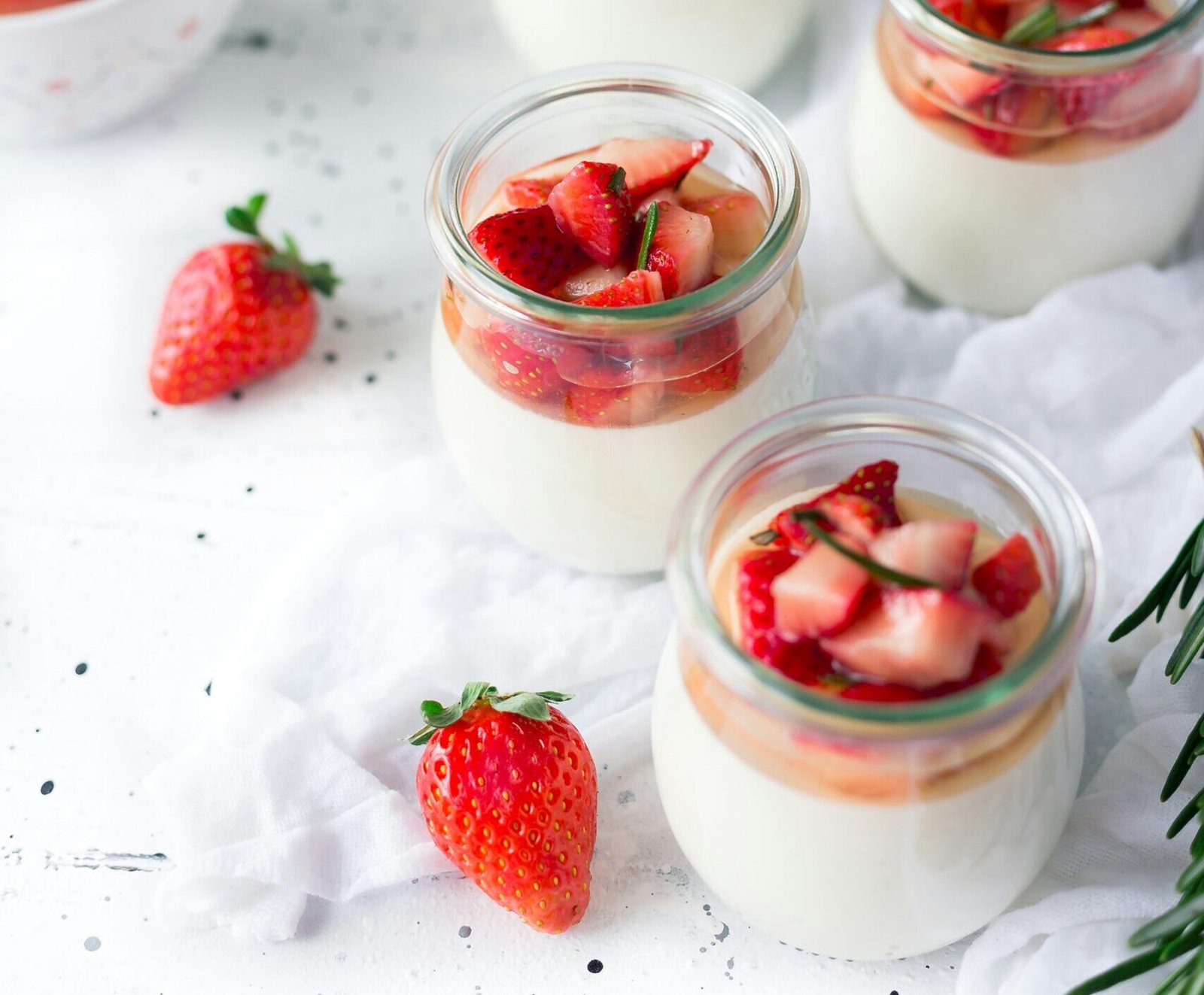 zdjęcie deserów bez laktozy w przezroczystych słoiczkach z truskawkami utsawionych na jasnym stole