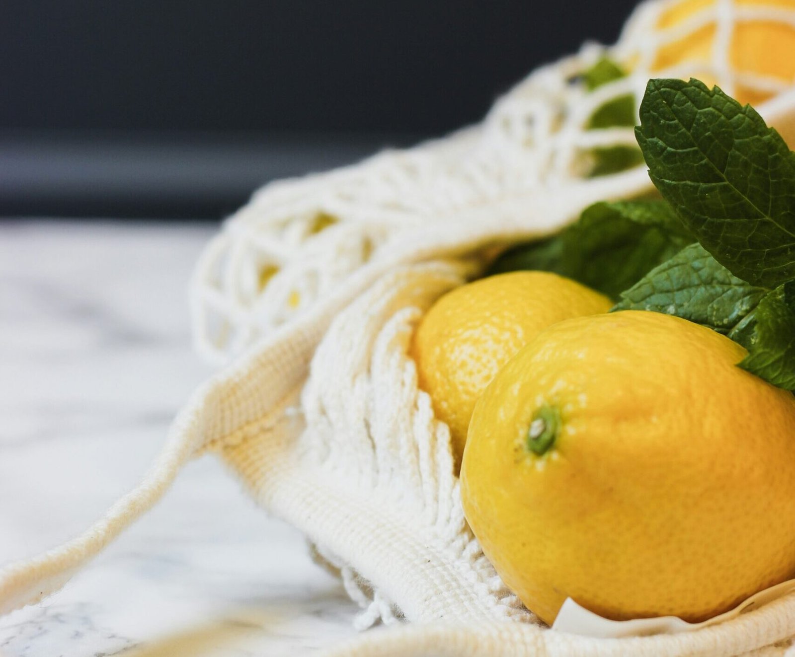 zdjęcie materiałowej siateczkowej torby na zakupy z cytrynami i miętą w środku upołożonej na marmurowym blacie