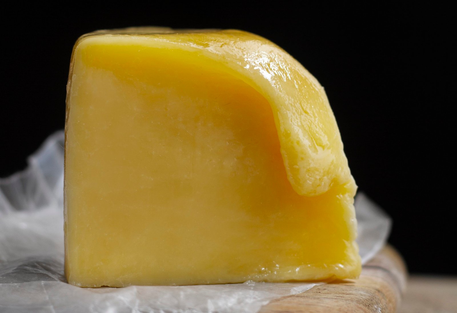 Blok żółtego masła klarowanego na papierze pergaminowym, z lekko stopioną i błyszczącą powierzchnią.