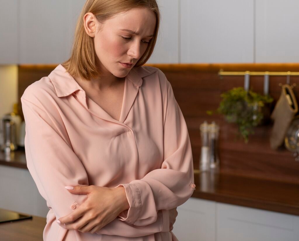 młoda kobieta stoi w kuchni z pochyloną głową i trzyma się za brzuch z powodu nietolerancji laktozy