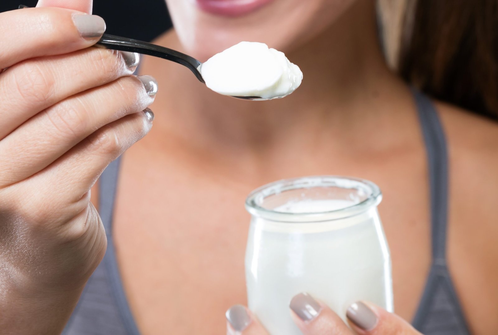 Kobieta jedząca odżywkę białkową w formie jogurtu z małego słoiczka, trzymając łyżeczkę z porcją białej masy.