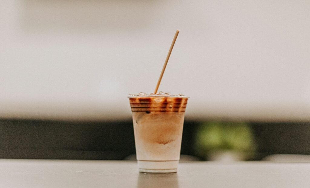 zdjęcie kawy z mlekiem bez laktozy w plastikowym kubeczku z papierową słomką