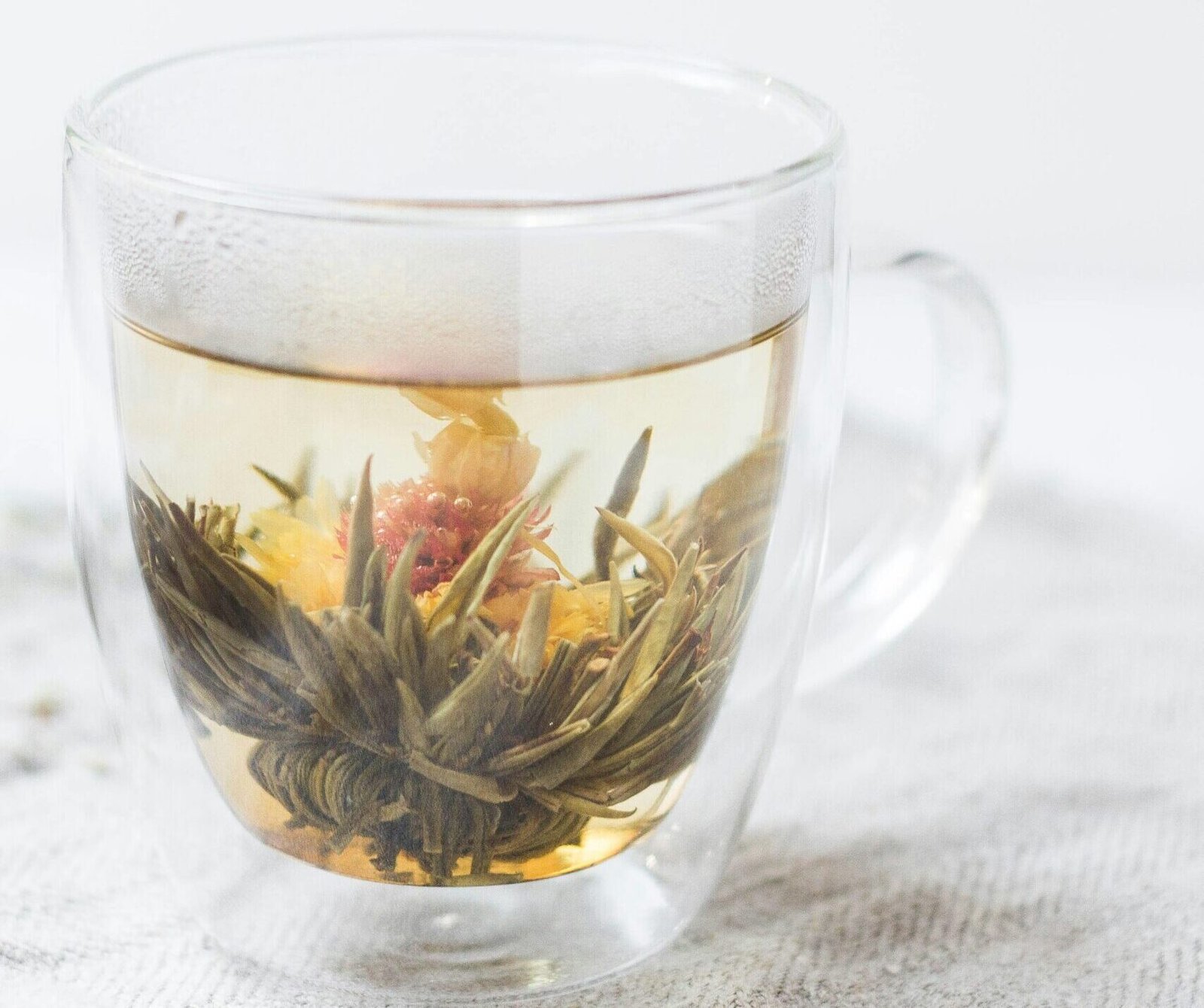 zdjęcie przezroczystego kubka z ziołami, które rozkwitają pod wpływem gorącej wody, ustawionego na jasnym stole