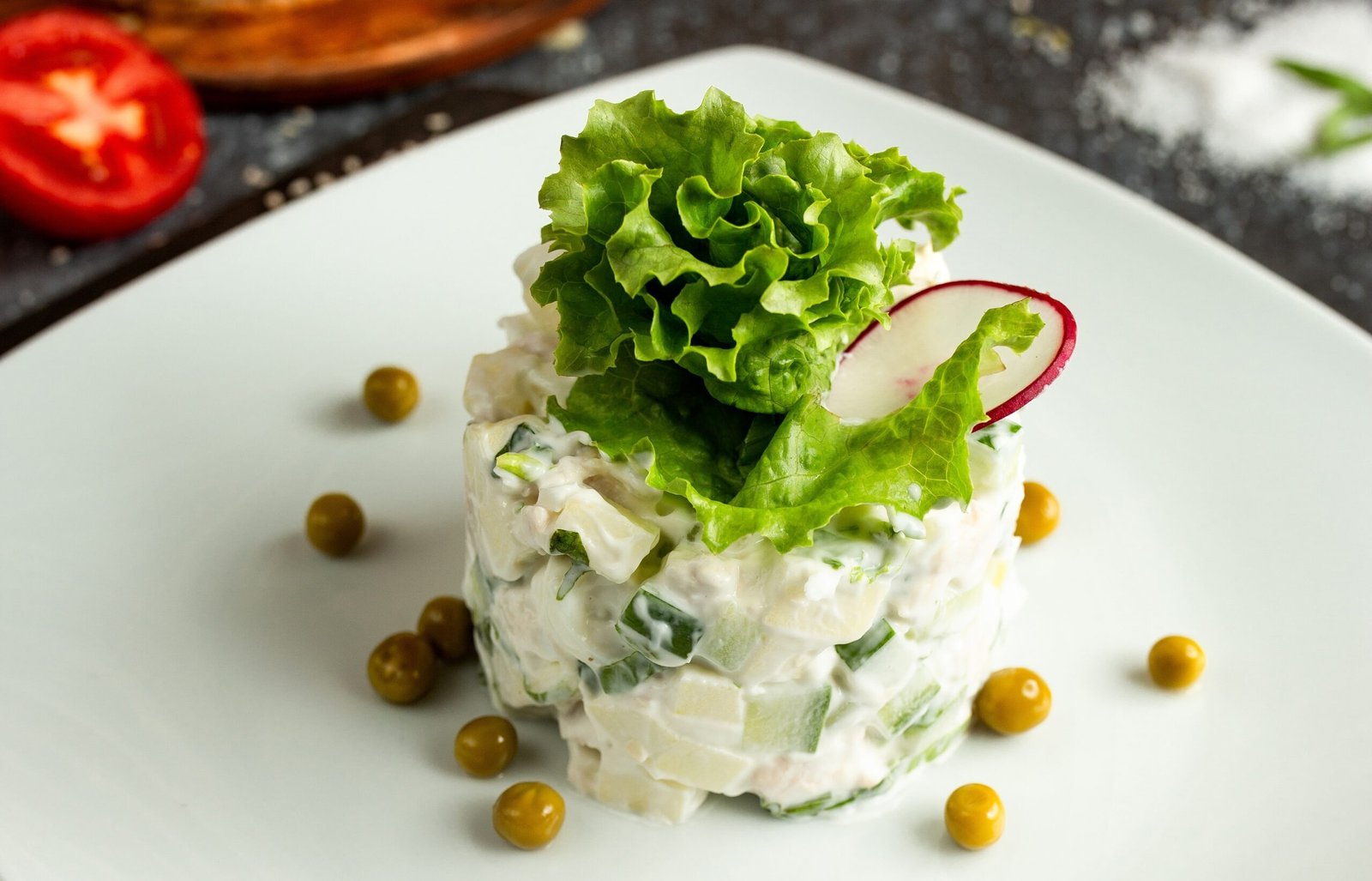 sałatka warzywna z sosem bez laktozy, z liściem sałaty i rzodkiewką na górze, podane na białym talerzu, posypanym zielonym groszkiem