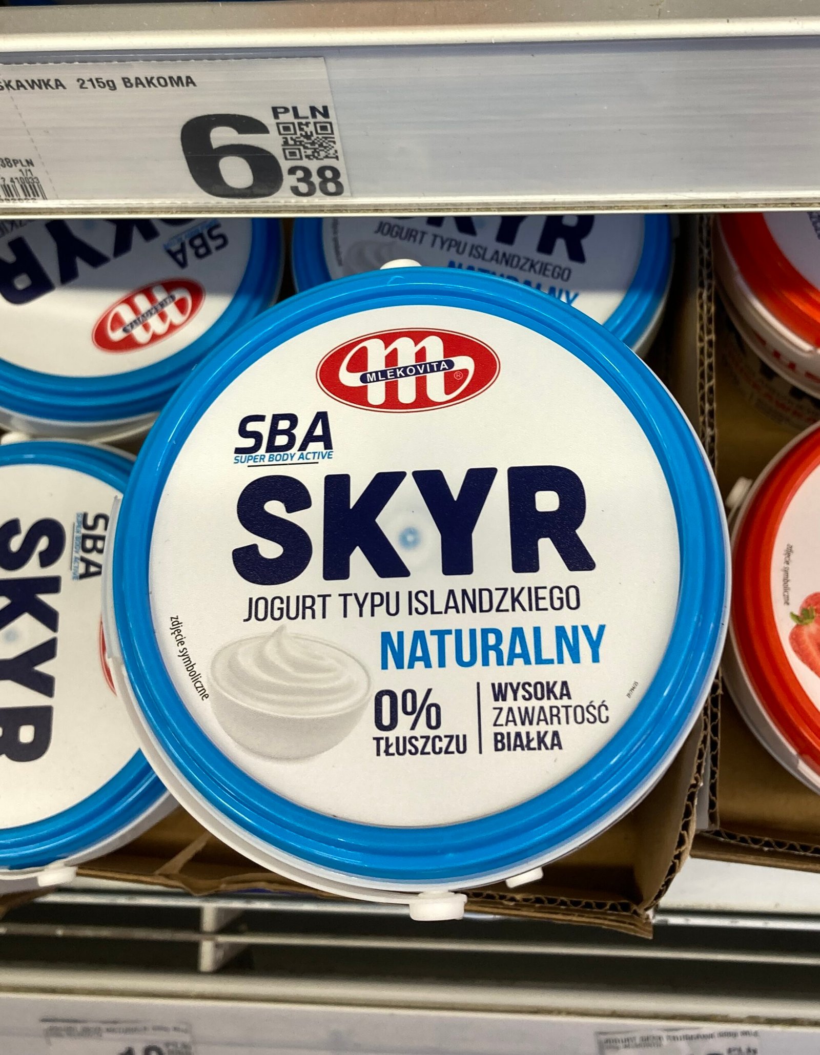 zdjęcie jogurtu skyr w opakowaniu typu wiaderko na tle sklepowej lodówki