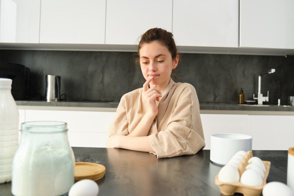 nietolerancja laktozy a skaza białkowa Kobieta siedząca w kuchni i zastanawiająca się nad wyborem produktów mlecznych – nietolerancja laktozy czy skaza białkowa?