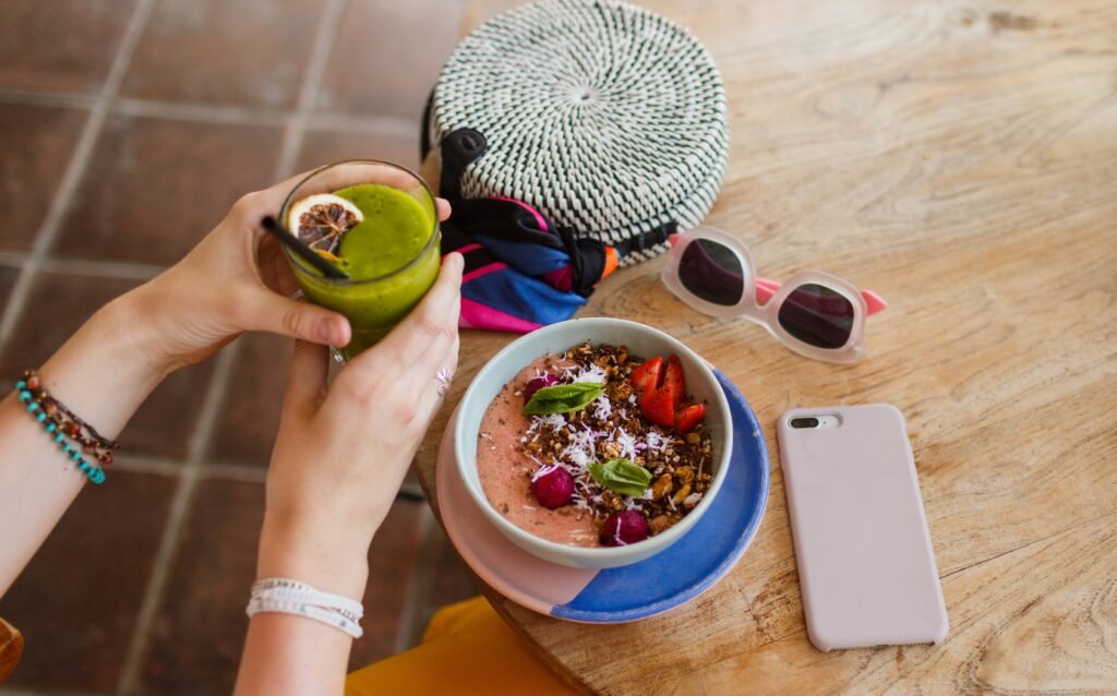 Nie daj się laktozie na wakacjach Kobieta na wakacjach trzyma zielony koktajl i je smoothie bowl bez laktozy – zdrowe śniadanie dla osób z nietolerancją laktozy.