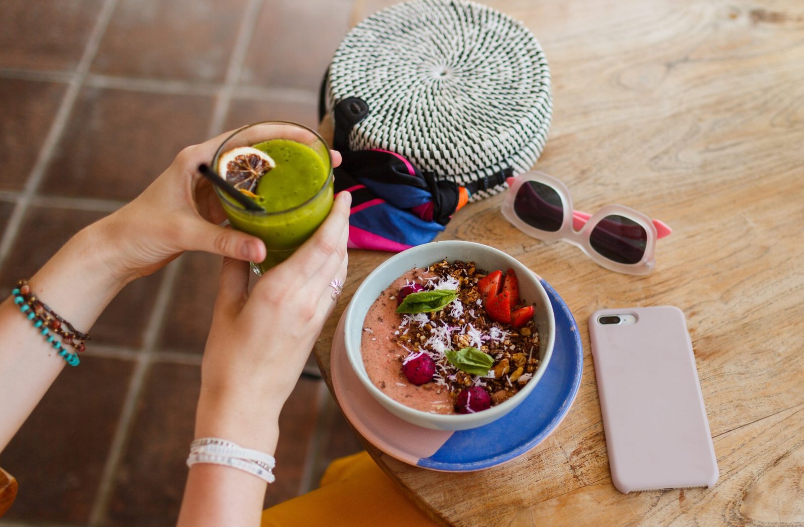 Kobieta na wakacjach trzyma zielony koktajl i je smoothie bowl bez laktozy – zdrowe śniadanie dla osób z nietolerancją laktozy.